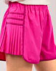 Women wearing hot pink pleated athletic shorts styled for athleisure fashion