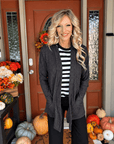 Woman wearing a heathered black open front cardigan over a striped top with black pants for a casual layered outfit.