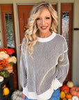 Woman wearing a cream and dark brown two tone ribbed crewneck sweater with long sleeves, contrast trim, and blue jeans.