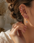 Woman wearing an 18K gold dipped blush clover earring set featuring pearl studs, gold hoops, pavé huggies, and clover drop earrings.