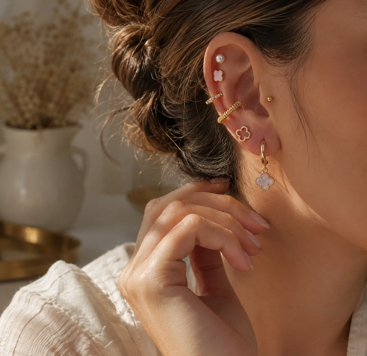 Woman wearing an 18K gold dipped blush clover earring set featuring pearl studs, gold hoops, pavé huggies, and clover drop earrings.