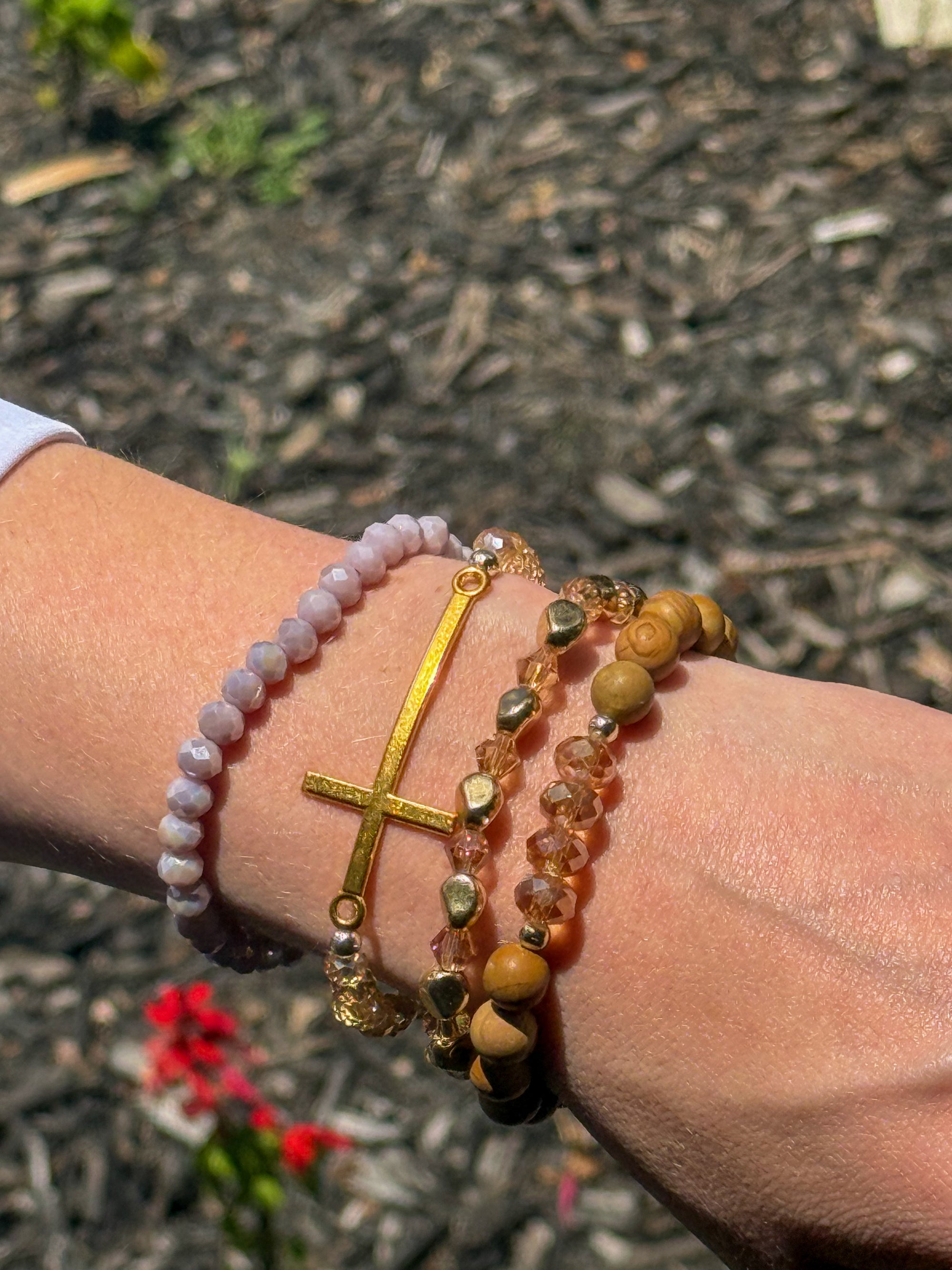 Christian bracelet stack featuring a horizontal gold cross with crystal and wood bead stretch bracelets.