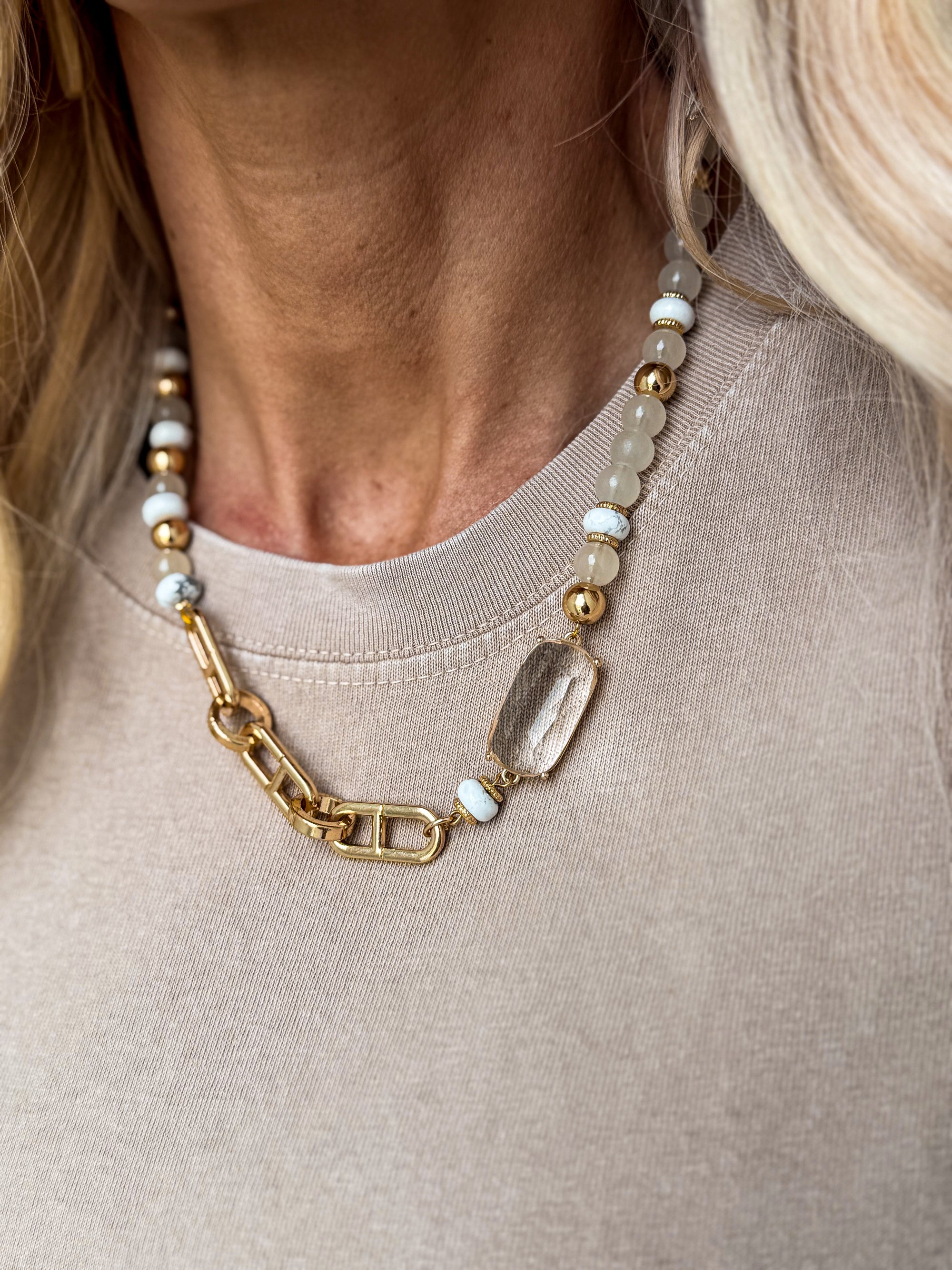 close-up of gold mixed chain and bead statement necklace with neutral stones styled on a beige top