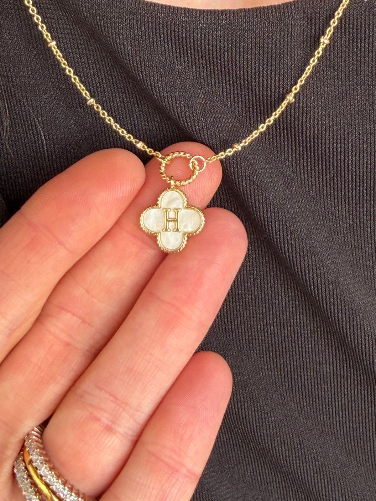 Gold monogram necklace with a mother-of-pearl clover pendant, initial centerpiece, and dainty satellite chain.