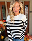 Woman wearing a black and white striped knit crewneck sweater with a pearl-embellished bow detail, styled with blue jeans.
 Copy