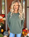Woman wearing a sage green French terry pullover with ribbed neckline, long sleeves, side pockets, and blue jeans.
