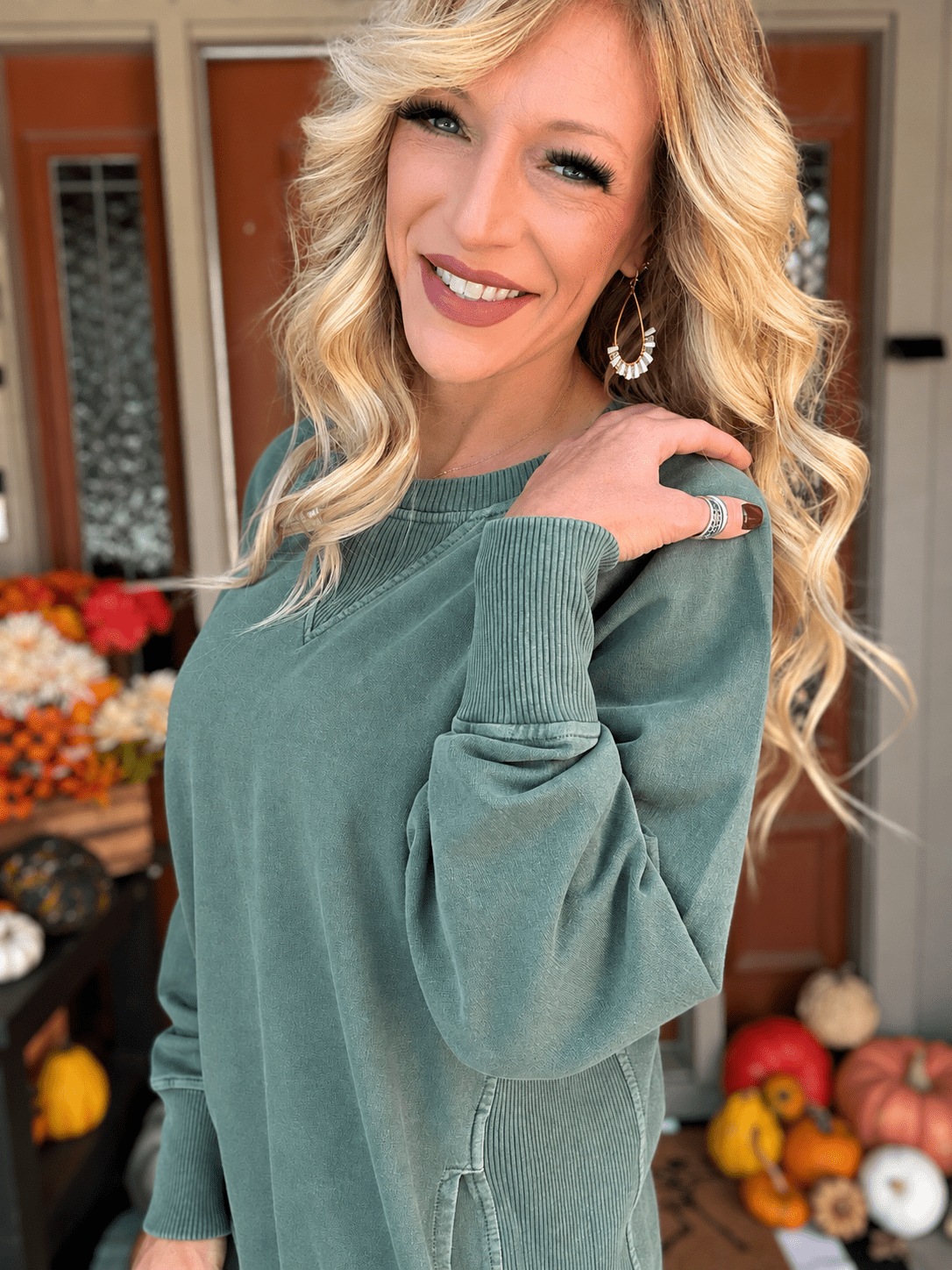 Close-up of sage green cotton French terry pullover showing ribbed sleeve cuff, V-shaped neckline detail, and side pocket.
