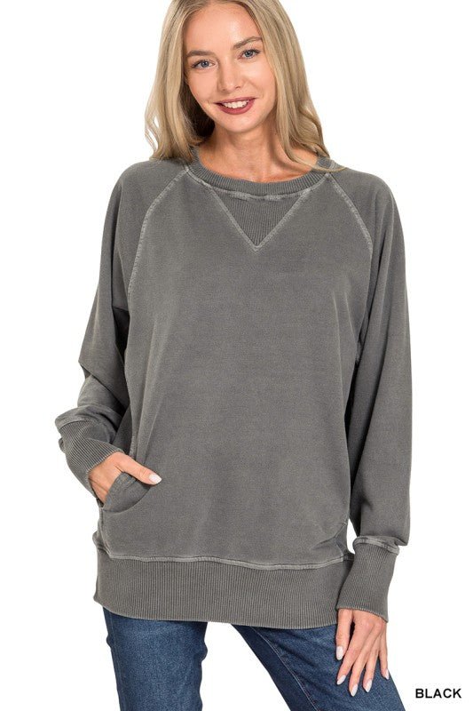 Woman modeling a pigment-dyed black cotton French terry sweatshirt with V-shaped ribbed neckline detail, raglan sleeves, and pockets.