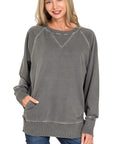 Woman modeling a pigment-dyed black cotton French terry sweatshirt with V-shaped ribbed neckline detail, raglan sleeves, and pockets.