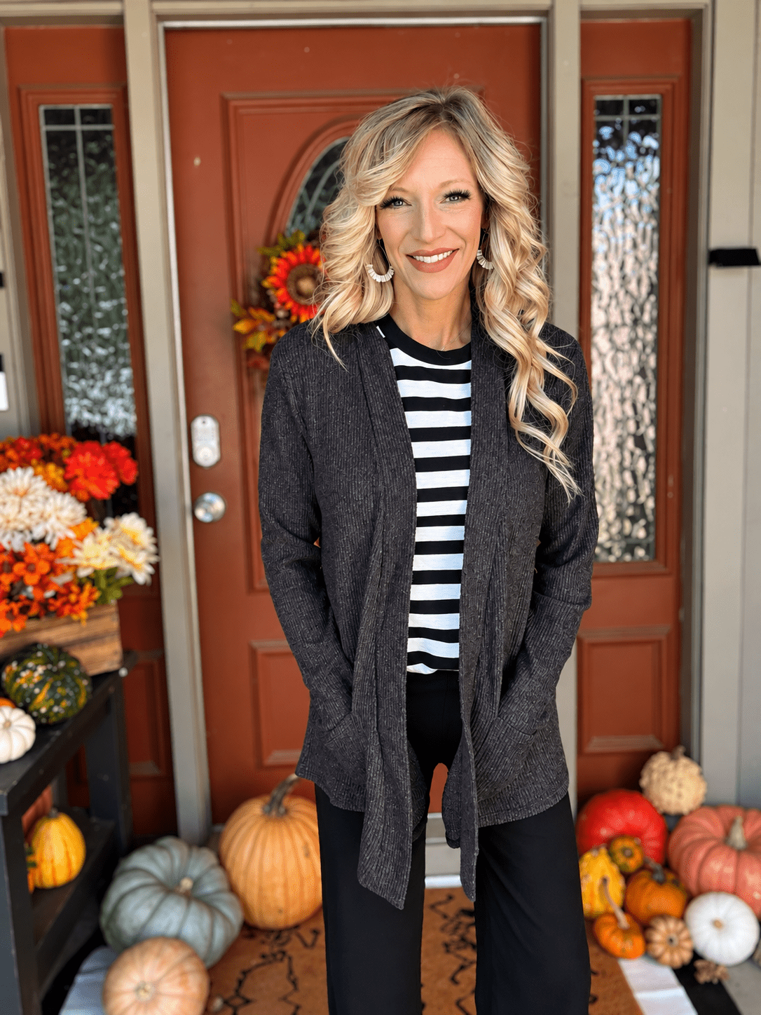 Woman wearing a heathered black open front cardigan over a striped top with black pants for a casual layered outfit.