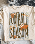 Cream Comfort Colors® Football Season graphic tee featuring vintage football artwork, distressed lettering, orange bows, and a relaxed unisex fit.