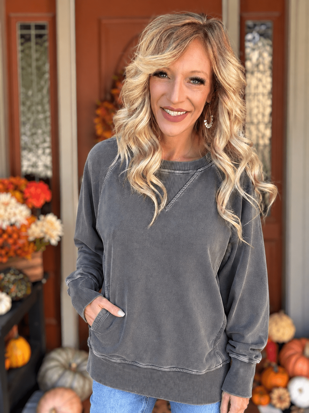 Woman wearing a washed black French terry pullover with ribbed neckline, long sleeves, and side pockets, styled with blue jeans.