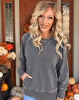 Woman wearing a washed black French terry pullover with ribbed neckline, long sleeves, and side pockets, styled with blue jeans.
