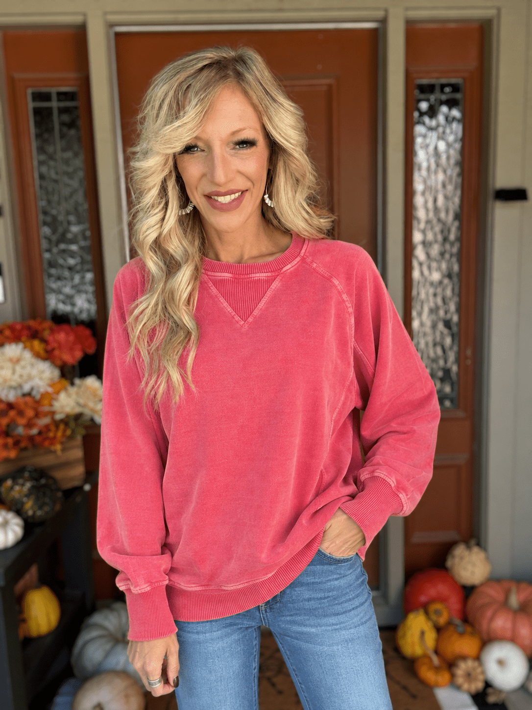 Woman modeling a pigment-dyed dark red cotton sweatshirt with long sleeves, ribbed cuffs, and blue denim jeans.