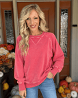 Woman modeling a pigment-dyed dark red cotton sweatshirt with long sleeves, ribbed cuffs, and blue denim jeans.