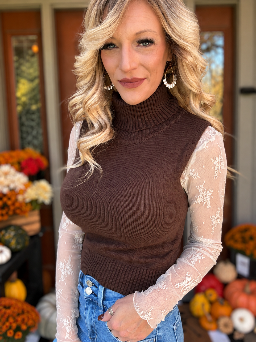 Light mocha sheer floral lace top styled underneath a brown sleeveless turtleneck sweater with blue jeans, showing floral lace sleeves.