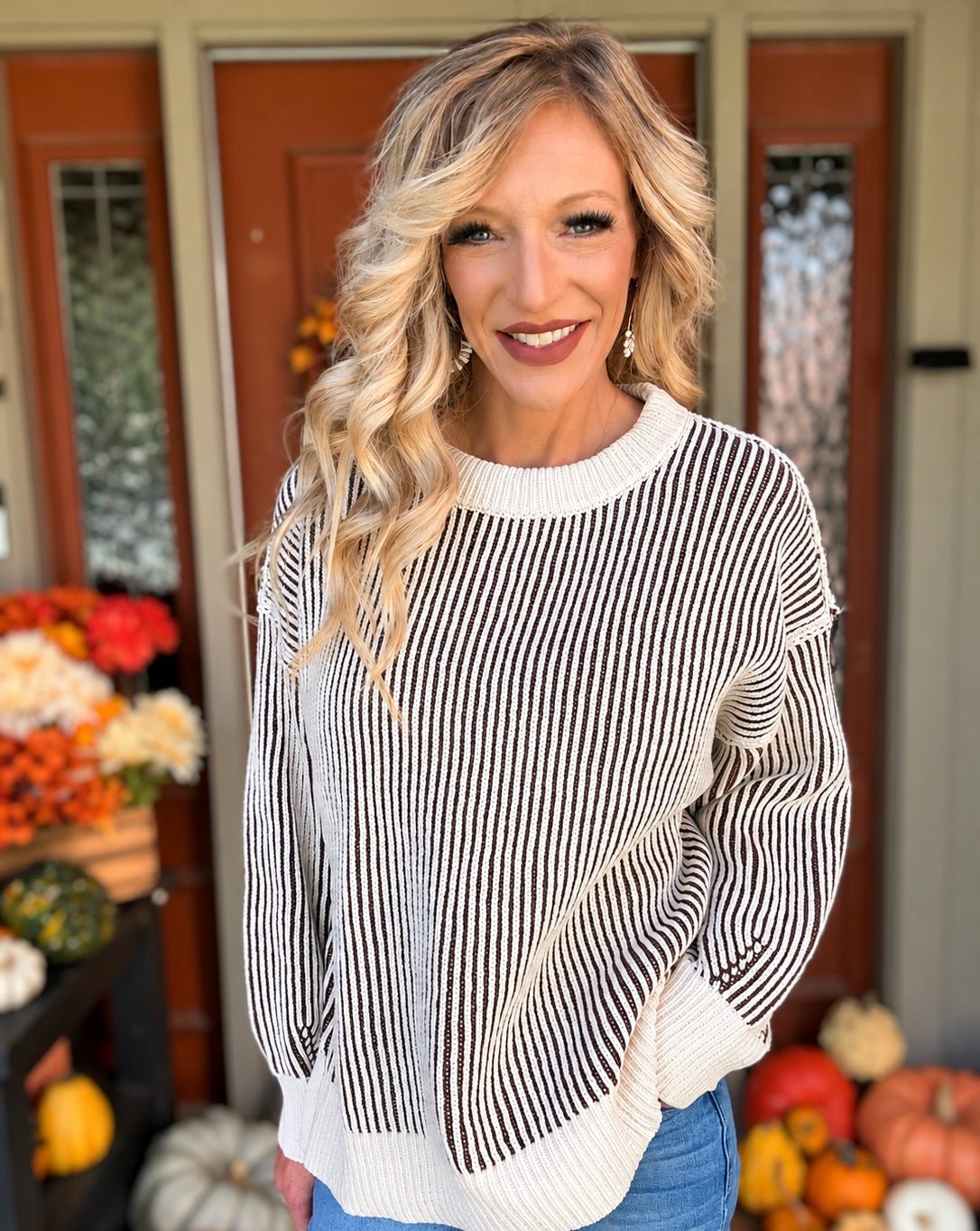 Woman wearing a cream and dark brown two tone ribbed crewneck sweater with long sleeves, contrast trim, and blue jeans.
 