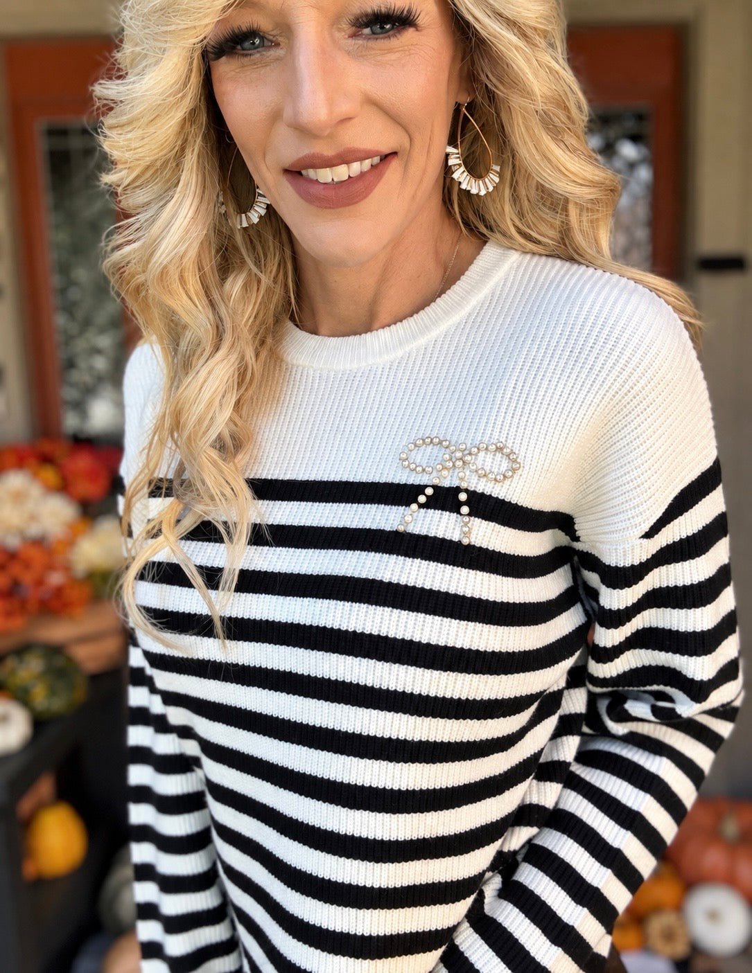 Close-up of a black and white ribbed knit sweater showing horizontal stripes, a white crew neckline, and a pearl-embellished bow on the chest.