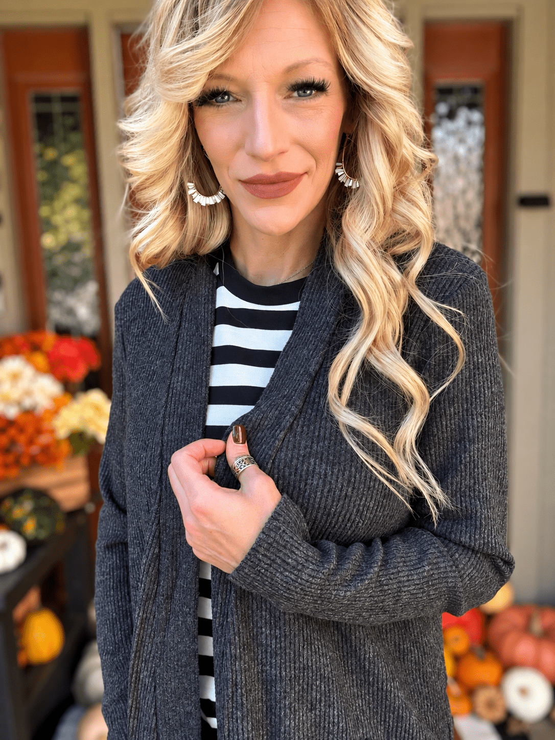 Woman wearing a textured black ribbed cardigan layered over a black and white striped shirt, showing the front opening and sleeve detail.