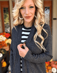 Woman wearing a textured black ribbed cardigan layered over a black and white striped shirt, showing the front opening and sleeve detail.