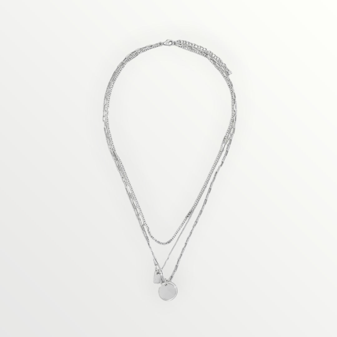 Triple-layer silver necklace with paperclip chain, delicate chain, circle charm, and tag pendant.