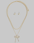 Layered gold necklace featuring an oval bead chain, crystal bow pendant, matching crystal stud earrings, and adjustable extender.
