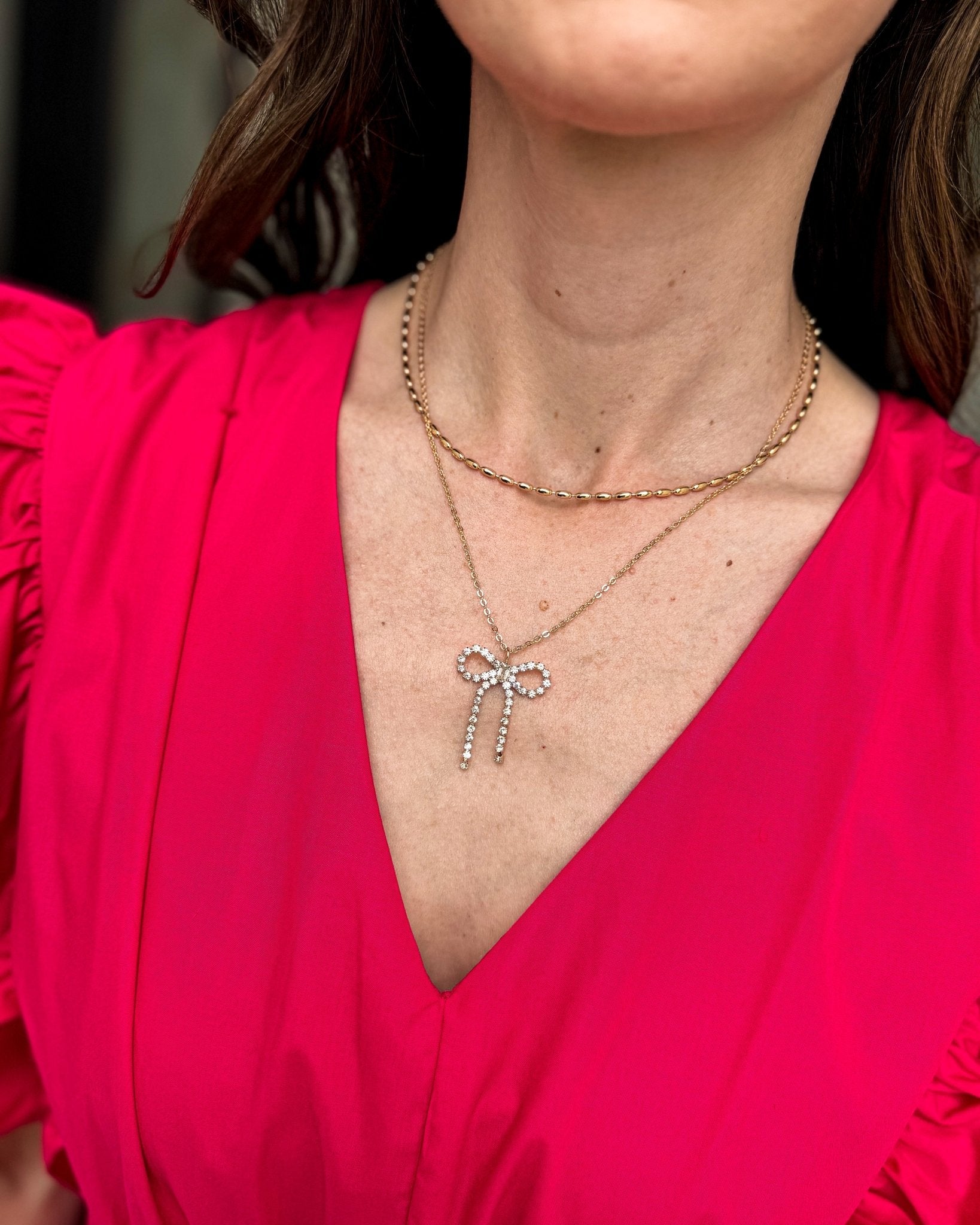 Layered gold-tone necklace with sparkling crystal bow pendant and coordinating crystal stud earrings.